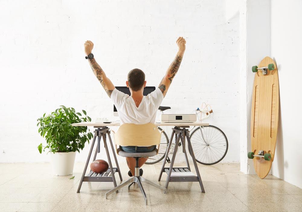 A man with arms raised, sitting at a desk in a room cooled without AC.